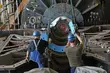 Two workers wearing safety helmets positioning a large metal component inside heavy industrial machinery.